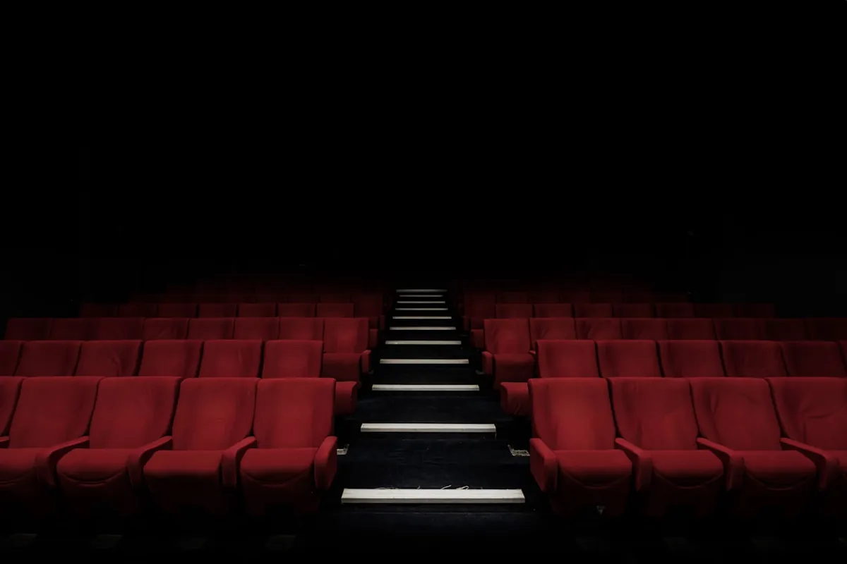Sala de cine en penumbra con butacas rojas frente a la pantalla